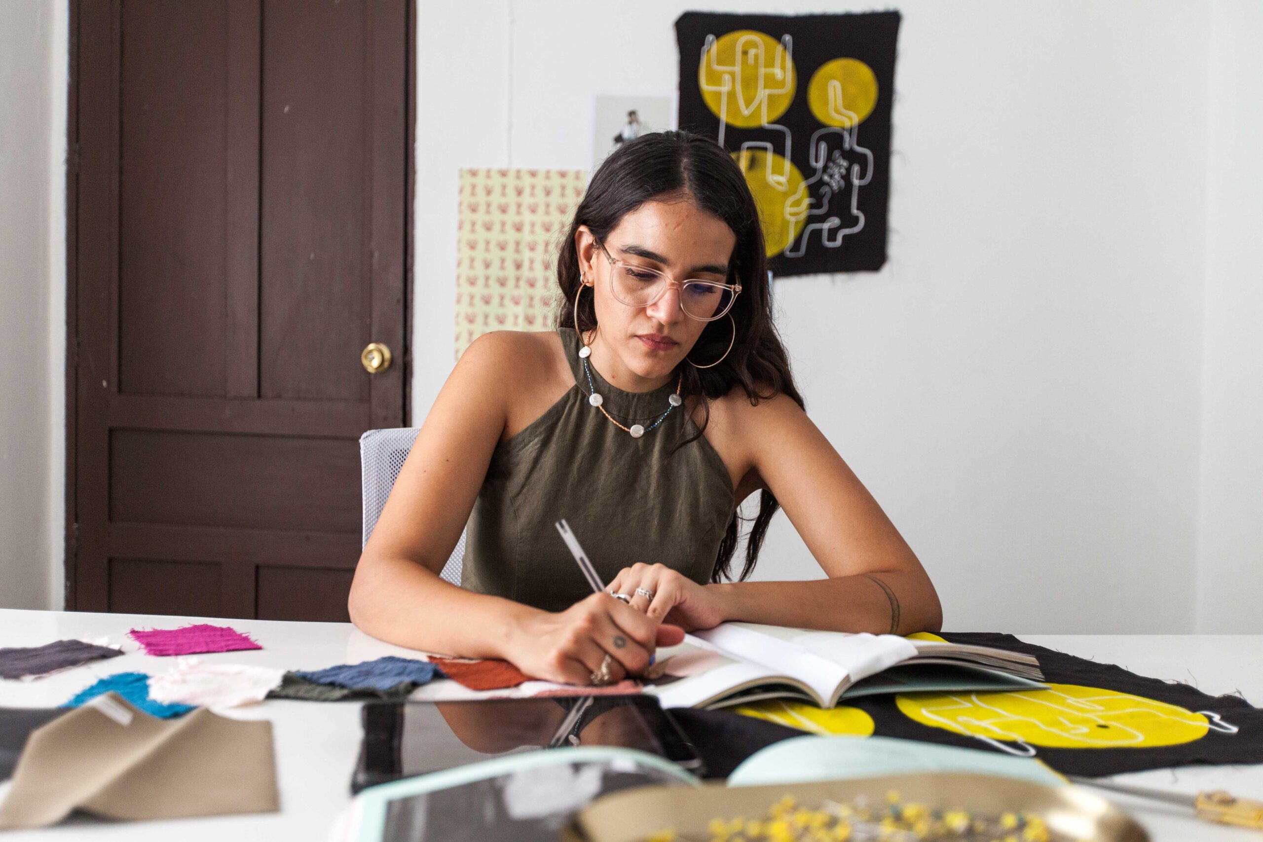 A fashion designer drawing/writing on a notebook, surrounded by fabric samples